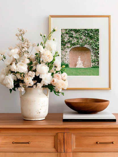 Feminine garden wall art showing a statue beneath an arched stone wall with greenery and soft tones.