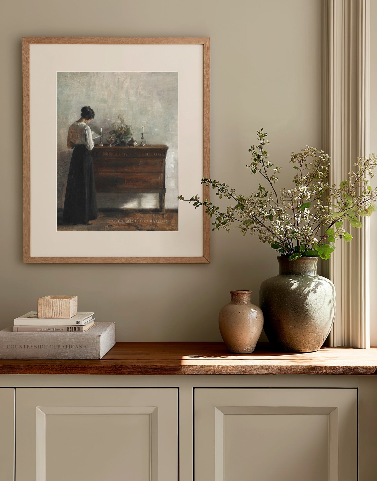 Framed vintage artwork on a wall above a wooden cabinet with decorative items.